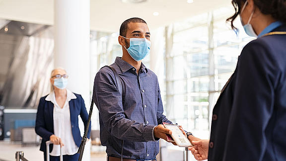 Herr mit Maske zeigt sein Handy an der Einlasskontrolle vor. Dieses wird von einer Frau mit Maske kontrolliert.